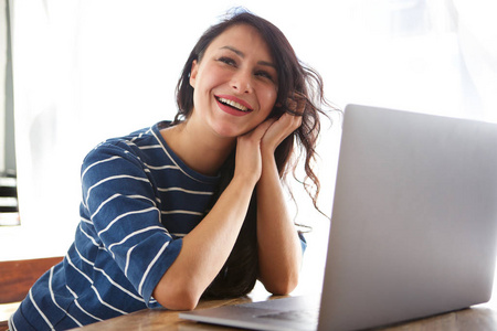 美丽的女人笑着坐在桌旁，手提电脑