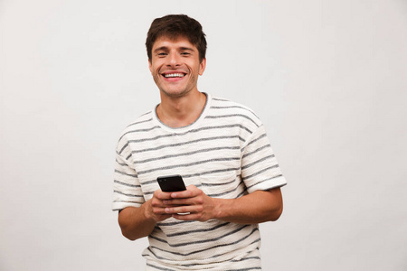 快乐开朗英俊的男人用手机站在白色背景墙上孤立的形象。
