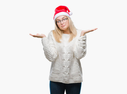 年轻的高加索女人戴着圣诞帽，在孤立的背景上毫无头绪，表情混乱，举起手臂和手。 怀疑概念。
