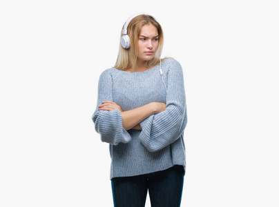 年轻的高加索女人听音乐时戴着耳机，而不是孤立的背景怀疑论者，紧张的不赞成的表情出现在交叉的手臂上。 消极的人。