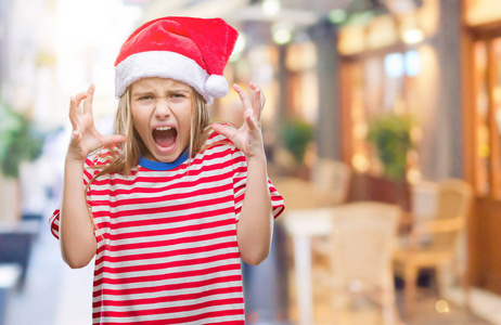 年轻漂亮的女孩戴着圣诞帽，在孤立的背景上疯狂和疯狂地大喊大叫，咄咄逼人的表情和手臂抬起。 挫折概念。