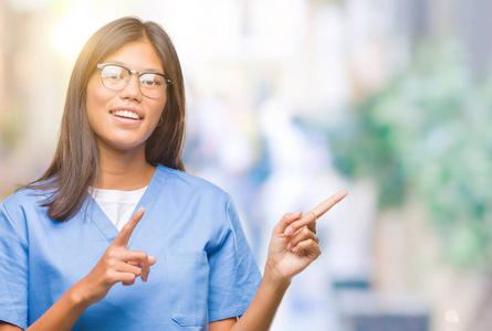 年轻的亚洲医生女人在孤立的背景上微笑，看着相机，用两只手和手指指向一边。