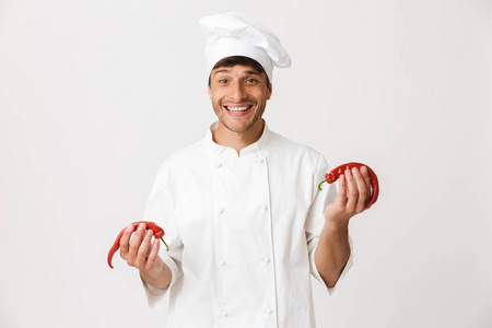 幸福的年轻厨师形象站在白色墙壁背景上，手持辣椒。