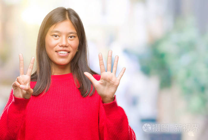 年轻的亚洲女人穿着冬天的毛衣，在孤立的背景上，用手指第七，微笑着自信和快乐。