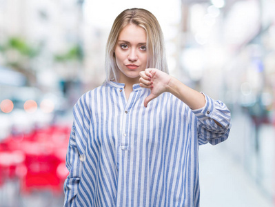 年轻的金发女人在孤立的背景上看起来不高兴和愤怒，表现出拒绝和消极的拇指向下的手势。 不好的表情。