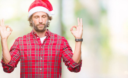 英俊的西班牙男子模特穿着圣诞老人的圣诞老人在孤立的背景下放松和微笑，闭着眼睛，用手指做冥想手势。 瑜伽概念。