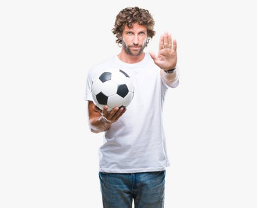 英俊的西班牙裔男子模型，用张开的手在孤立的背景上举着足球球，用严肃而自信的表情做停止标志