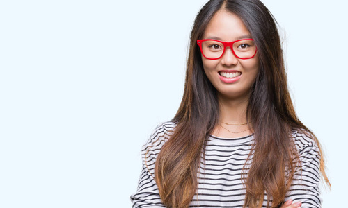 年轻的亚洲女人戴着眼镜，在孤立的背景上，快乐的脸，笑着交叉的手臂看着相机。积极的人。