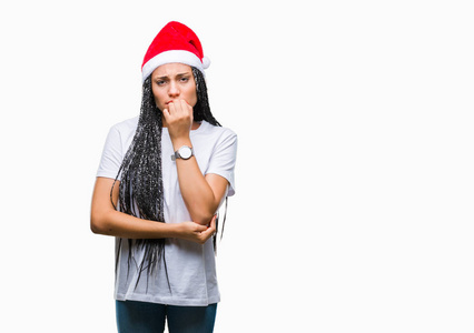 年轻的发辫非洲裔美国女孩戴着圣诞帽在孤立的背景看起来压力和紧张，双手咬嘴指甲。焦虑问题。