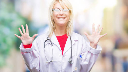 年轻漂亮的金发医生女士穿着医疗制服，在孤立的背景下，用手指10号，微笑着自信和快乐。