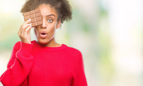 年轻的美国黑人妇女在孤立的背景下吃巧克力棒，吓得满脸惊讶，恐惧和兴奋