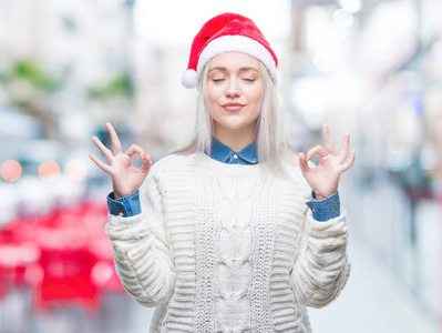 年轻的金发女子戴着圣诞帽在孤立的背景下放松和微笑，闭着眼睛做冥想手势与手指。瑜伽概念。
