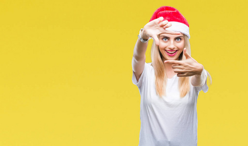 年轻美丽的金发女子圣诞帽在孤立的背景微笑制作框架与手和手指与快乐的脸。创意和摄影理念..
