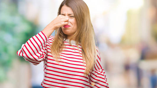 年轻漂亮的女人随意的条纹冬天的毛衣在孤立的背景上闻到一些臭味和恶心，难以忍受的气味，用手指在鼻子上屏住呼吸。坏气味的概念。