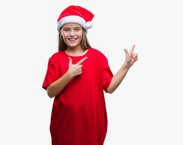 年轻漂亮的女孩戴着圣诞帽在孤立的背景上微笑着，看着相机，两只手和手指指向一边。