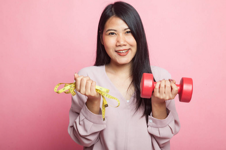健康的亚洲女人，带哑铃和粉红色背景的测量带