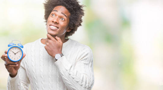 美国黑人男子抱着老式闹钟在孤立的背景下严肃的脸思考问题，很困惑的想法