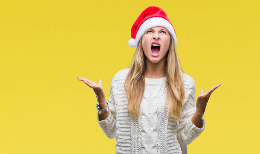 年轻漂亮的金发女人戴着圣诞帽，在孤立的背景上疯狂地大喊大叫，表情咄咄逼人，举起手臂。挫折的概念..