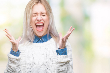 年轻的金发女人穿着冬天的毛衣，在孤立的背景上庆祝疯狂和惊讶的成功，举起手臂和睁开眼睛尖叫兴奋。赢家概念