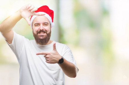 年轻的白种人嬉皮士戴着圣诞帽，在孤立的背景下微笑，用手和手指制作框架，用快乐的脸。创意和摄影理念..