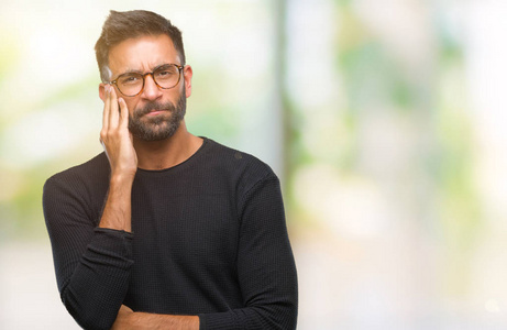 成年西班牙裔男子戴着眼镜，在孤立的背景下思考，看起来疲惫，厌倦了交叉双臂的抑郁问题。