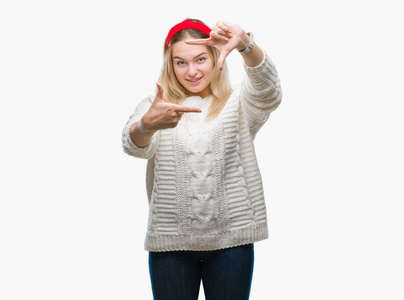 年轻的白种人女人穿着冬天的毛衣，在孤立的背景下微笑，用手和手指制作框架，用快乐的脸。创意和摄影理念..