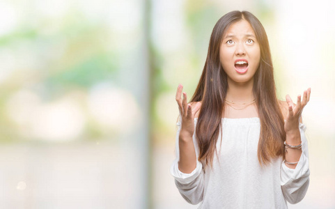 年轻的亚洲女人在孤立的背景下疯狂疯狂地大喊大叫，咄咄逼人的表情和手臂抬起。挫折的概念..