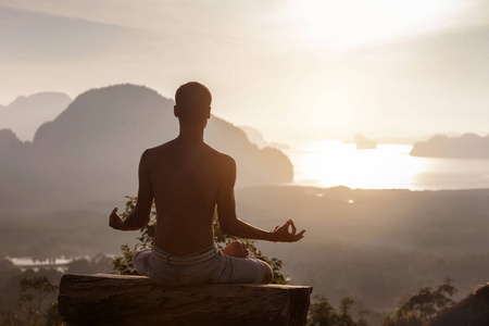 男子坐在瑜伽姿势在日出对海