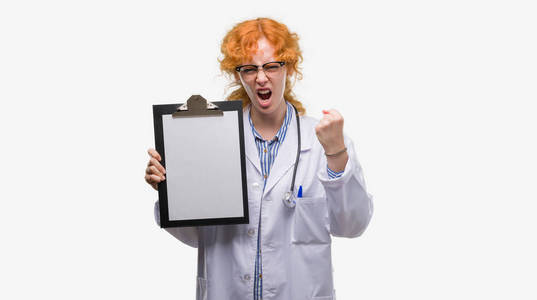 年轻的红发医生女人拿着剪贴板，生气和沮丧地大喊大叫，疯狂地举起手愤怒的概念