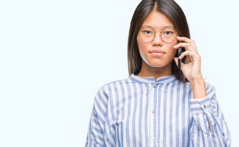 年轻的亚洲女人在电话上说话，背景偏僻，表情自信，聪明的脸，认真的思考