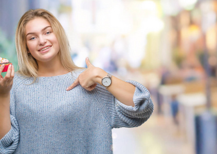 年轻的白种人女人在孤立的背景下吃甜蛋糕，惊讶的脸指着自己