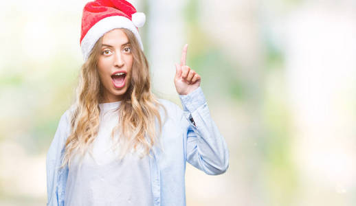 美丽的年轻金发女人戴着圣诞帽，在孤立的背景上指点着成功的想法。 退出并快乐。 一号。