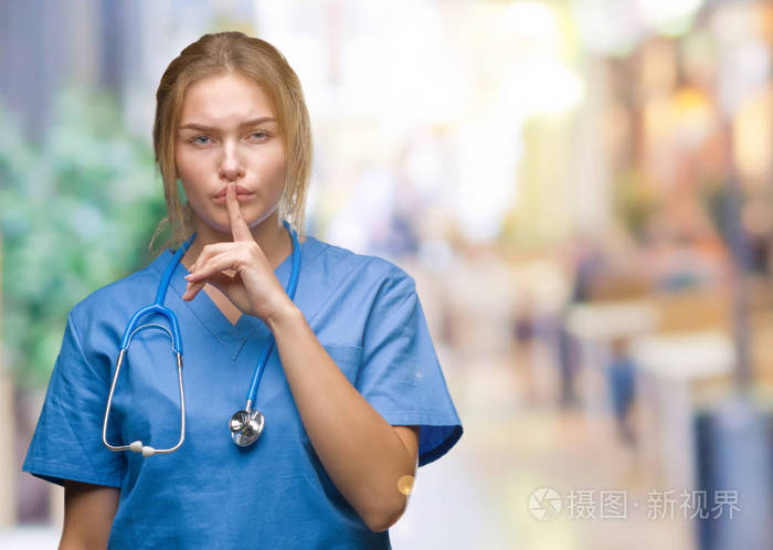 年轻的白种人医生女人穿着外科医生制服在孤立的背景上要求安静手指在