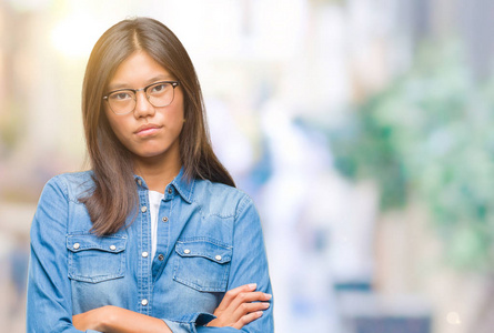 年轻的亚洲女人戴着眼镜，在孤立的背景怀疑和紧张的不赞成的表情在脸上交叉的手臂。 消极的人。