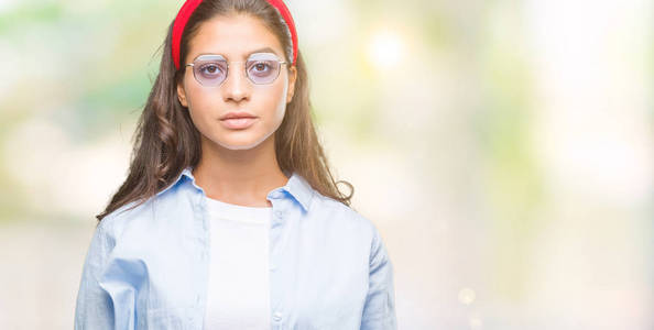 年轻漂亮的阿拉伯女人戴着太阳镜，在孤立的背景上，脸上有着严肃的表情。 简单自然地看着相机。