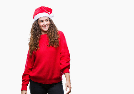 年轻的黑发女孩戴着圣诞帽，在孤立的背景上看着一边，脸上带着微笑，自然的表情。 自信地笑着。