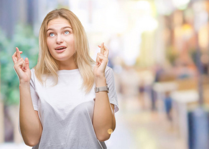 年轻的白种人女人在孤立的背景上微笑着交叉手指与希望和眼睛闭上。 运气和迷信的概念。