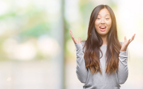 年轻的亚洲女人在孤立的背景下庆祝疯狂和惊讶的成功，举起手臂和睁开眼睛尖叫兴奋。 赢家概念