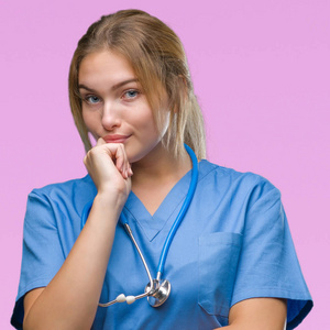 年轻的白种人医生女士穿着外科医生制服，在孤立的背景下，自信地看着相机，微笑着交叉的手臂和举起的手在下巴上。 积极思考。