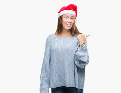 年轻美丽的高加索女人戴着圣诞帽，在孤立的背景上微笑，快乐的脸看着，用拇指指向一边。