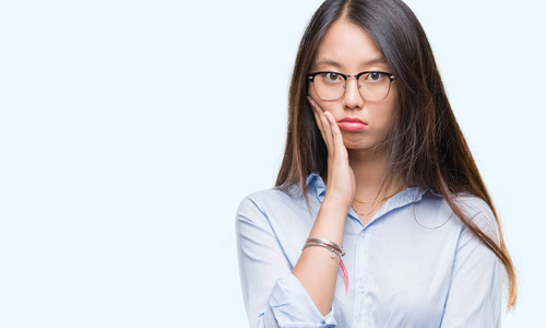 年轻的亚洲商界女性戴着眼镜，在孤立的背景下思考，看起来疲惫，厌倦了交叉双臂的抑郁问题。