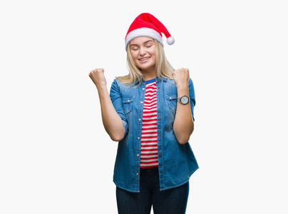 年轻的高加索女人戴着圣诞帽，在孤立的背景下，非常高兴和兴奋地做着胜利者的手势，举起手臂，微笑着，尖叫着，争取成功。 庆祝概念。