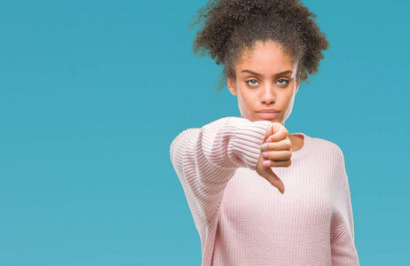 年轻的非洲美国女人穿着冬天的毛衣，在孤立的背景上看起来不高兴和愤怒，表现出拒绝和消极的拇指向下的手势。 不好的表情。