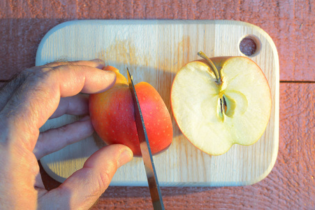 日落时分，用一把小刀在一块红棕色背景的木切割板上切苹果