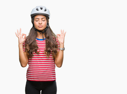年轻的阿拉伯骑自行车的女人戴着安全帽，在孤立的背景上放松，闭着眼睛微笑，用手指做冥想手势。 瑜伽概念。