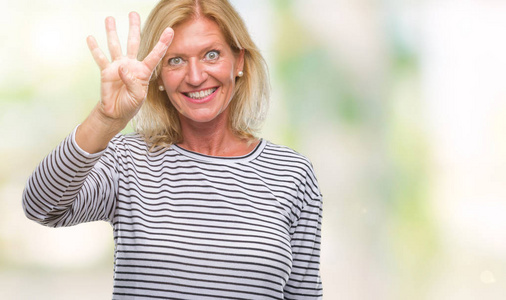 中年金发女人在孤立的背景上显示和指着第四个手指，同时微笑自信和快乐。