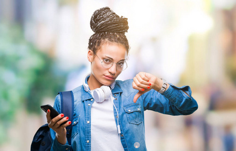 年轻的梳辫发非洲裔美国学生女孩使用智能手机在孤立的背景和愤怒的脸消极的迹象显示不喜欢拇指向下拒绝概念