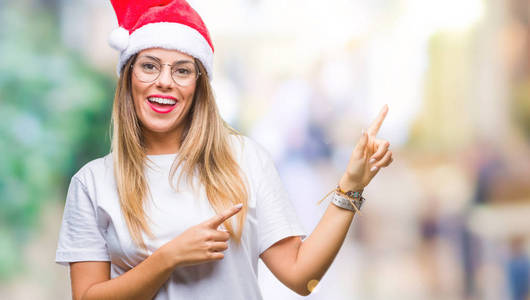 年轻漂亮的女人戴着圣诞帽，在孤立的背景上微笑着，看着相机，两只手和手指指向一边。