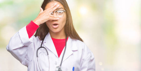 年轻的阿拉伯医生女人在孤立的背景下偷看，震惊地覆盖着脸和眼睛，用手透过手指看着尴尬的表情。