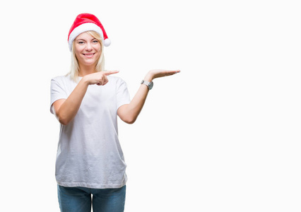 年轻漂亮的金发女人戴着圣诞帽，孤立的背景上惊讶和微笑的相机，同时呈现手和手指。